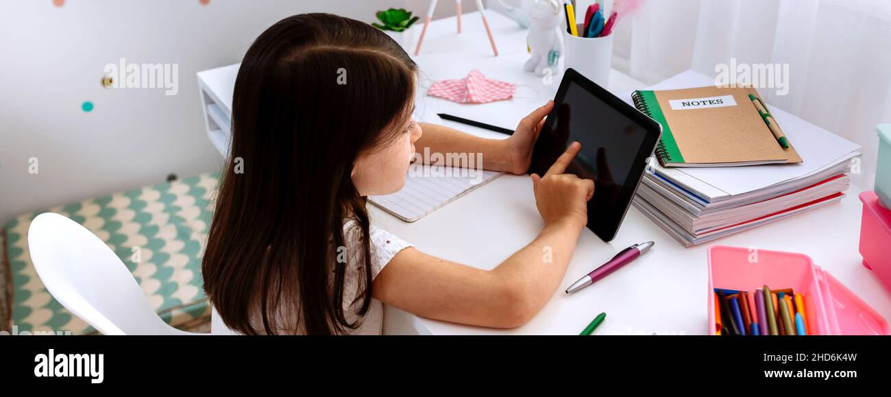 Ragazza che studia a casa con tablet e maschera sul tavolo Foto Stock