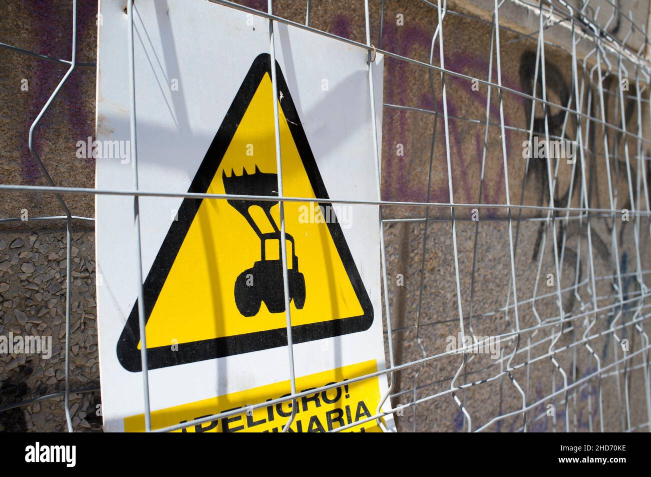 Segnale di avvertimento per macchine pesanti sul lavoro. Il caricatore frontale del trattore è visibile attraverso la recinzione. Foto Stock