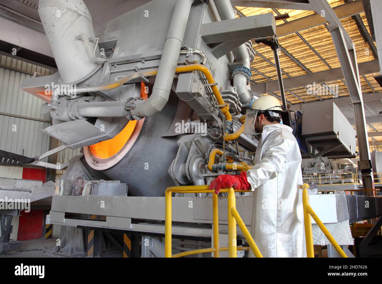 Riciclaggio dell'alluminio. Un uomo con indumenti protettivi e resistenti al calore monitora un forno di recupero dell'alluminio in funzione in un grande impianto di fusione. Foto Stock