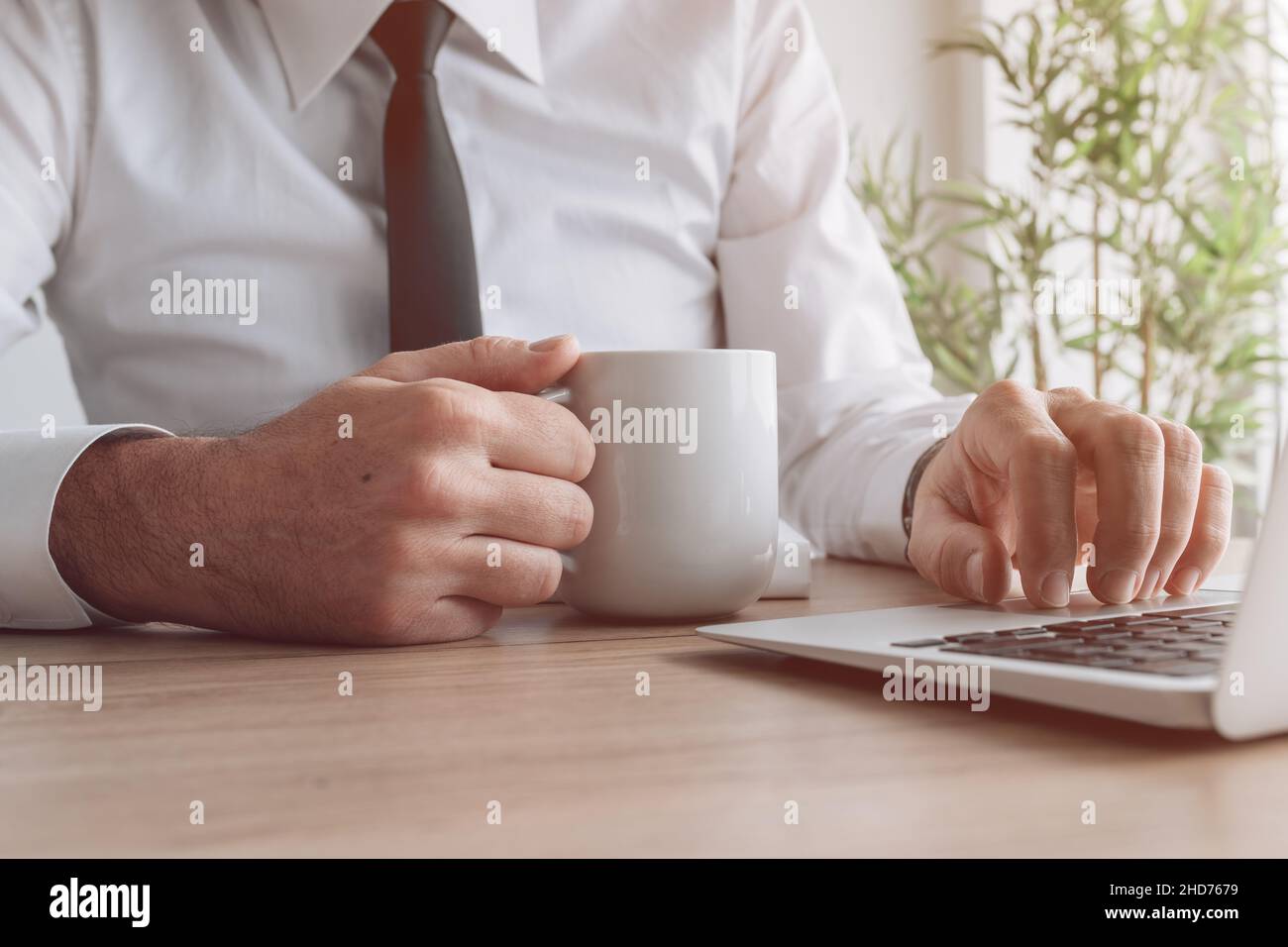 La giornata dell'ufficio inizia con un caffè, un uomo d'affari che tiene la tazza e usando il laptop, fuoco selettivo Foto Stock