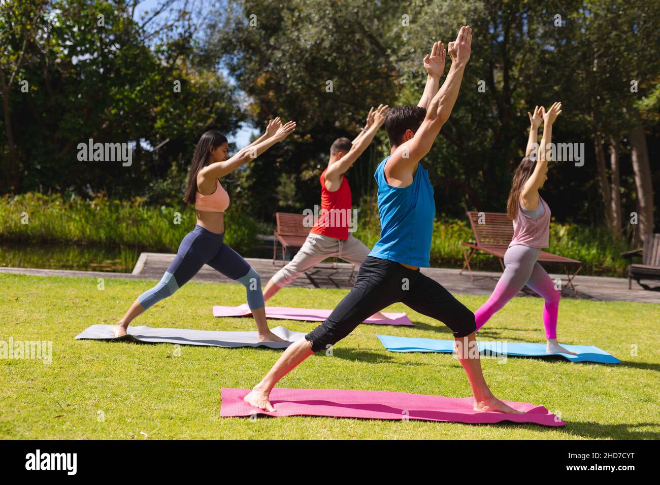 Intera lunghezza di uomini e donne con le braccia sollevate praticare yoga su materassini da ginnastica nel parco Foto Stock