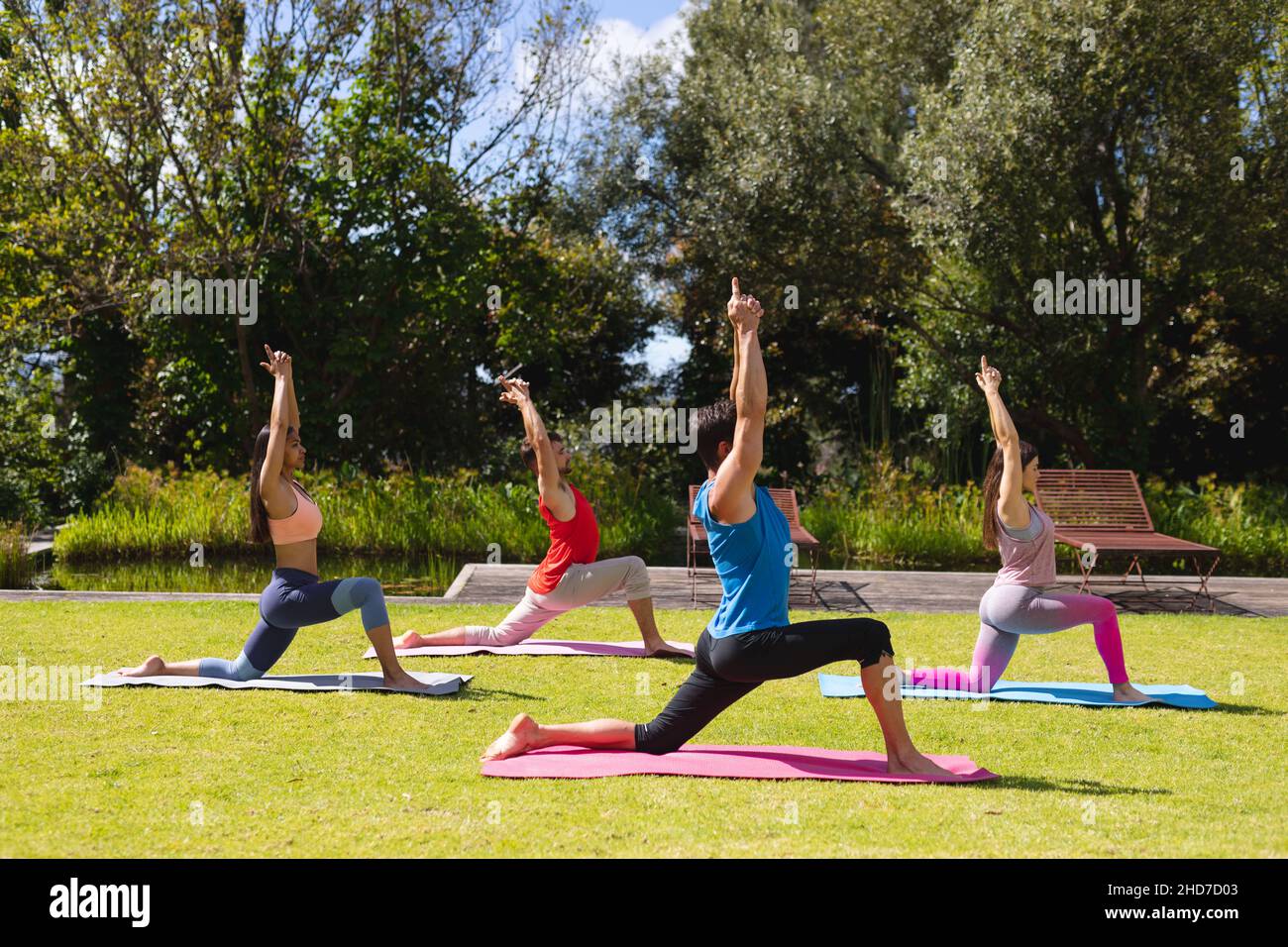 Uomini e donne con le braccia sollevate praticare yoga su materassini da ginnastica in parco il giorno di sole Foto Stock