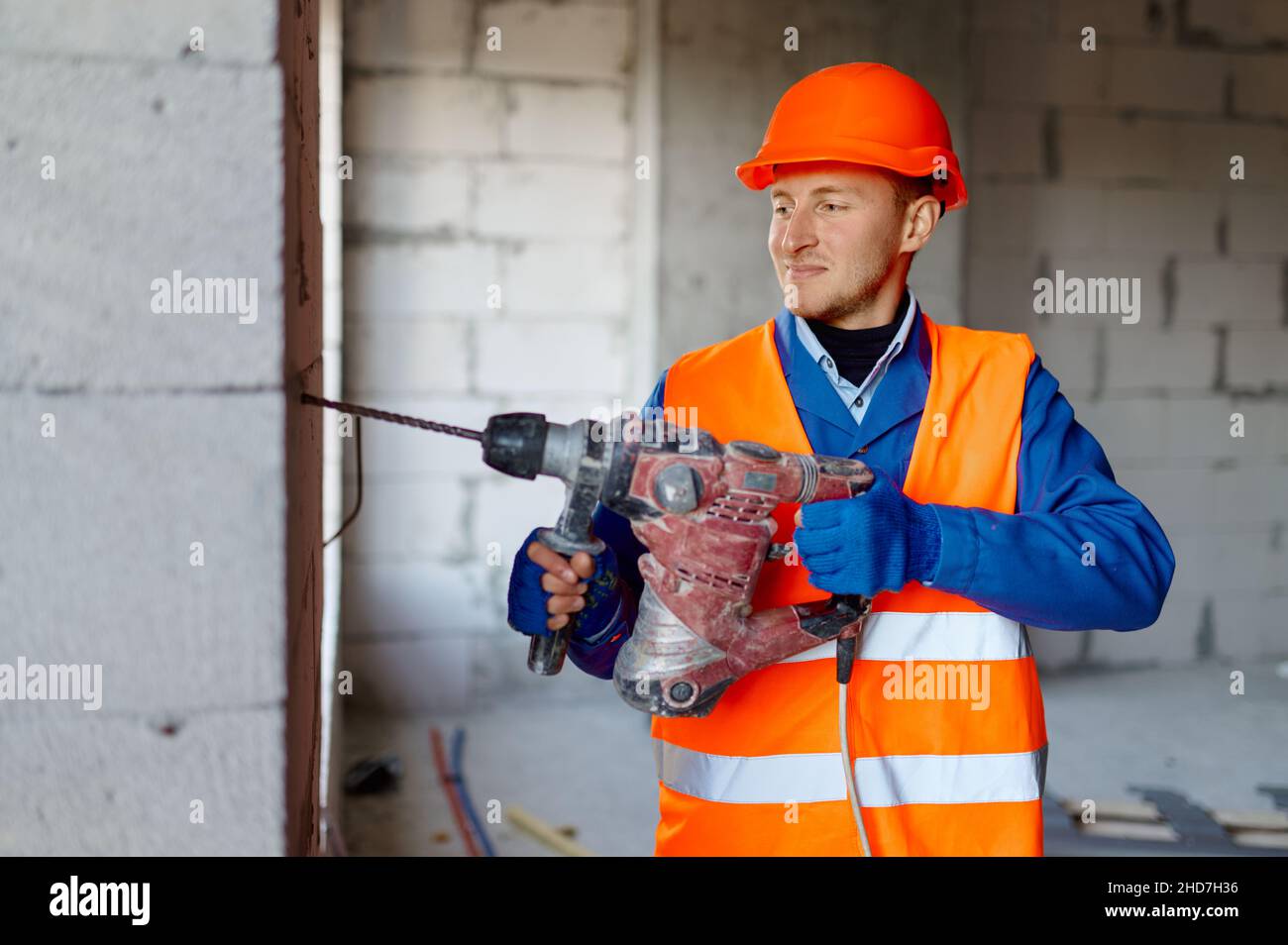 Costruttore in hardhat che lavora con il trapano in ambienti chiusi Foto Stock