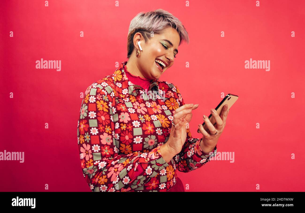 Sfogliare un'applicazione musicale molto diffusa. Giovane donna felice sorridendo allegro mentre tiene uno smartphone e indossa gli auricolari wireless. Giovane donna con ha tinto Foto Stock