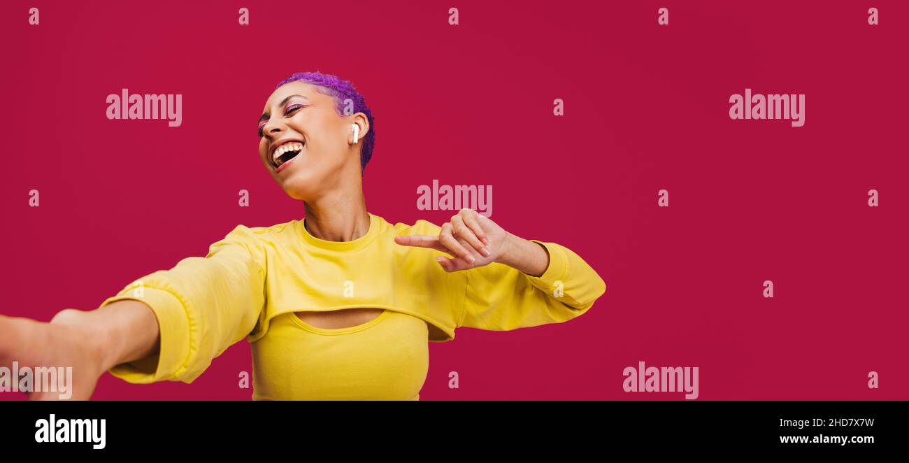 Giovane donna energica che balla alla sua canzone preferita. Giovane donna felice sorridendo allegro mentre indossano auricolari wireless in uno studio. Donna con pur Foto Stock