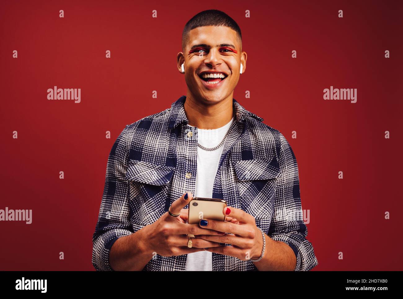 Ho la playlist migliore di sempre. Buon giovane uomo sorridente allegro mentre tiene uno smartphone e indossa le cuffie wireless. Giovane uomo alla moda enj Foto Stock