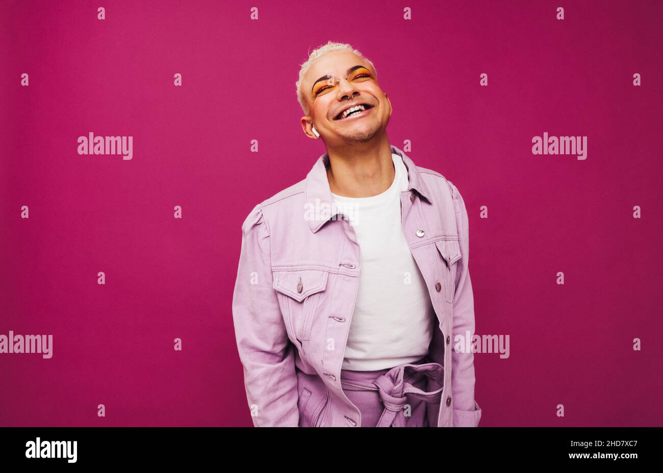 La musica mi rende felice. Queer man non conforme che sorride allegro mentre ascolta la sua playlist preferita utilizzando gli auricolari wireless. Spensierato giovane m Foto Stock