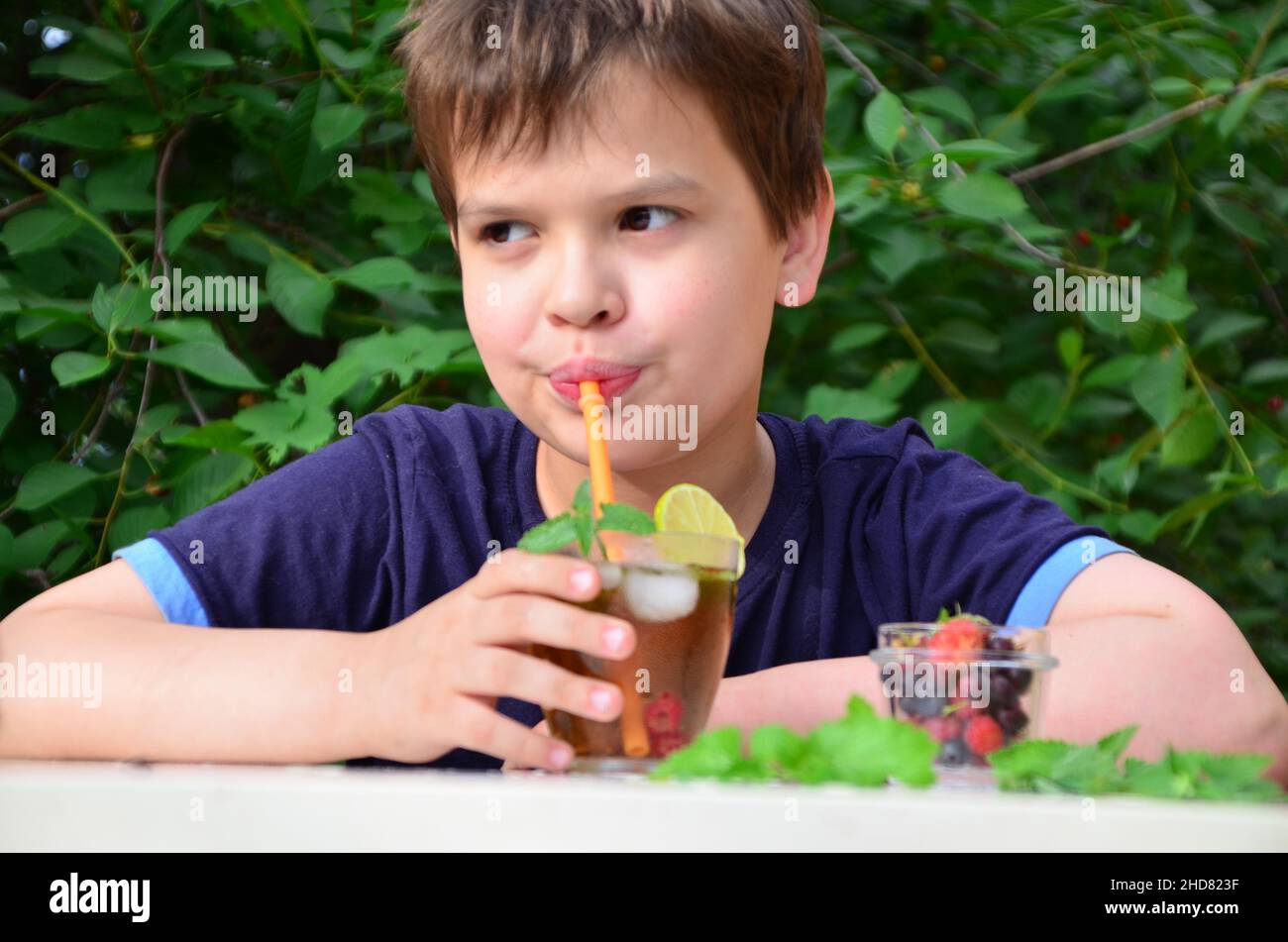 Bambino ragazzo drink naturale limonata bevanda estiva, tè con frutti di bosco, lime, lamponi e mirtilli, vacanza estiva nel parco. Rinfrescante naturale Foto Stock