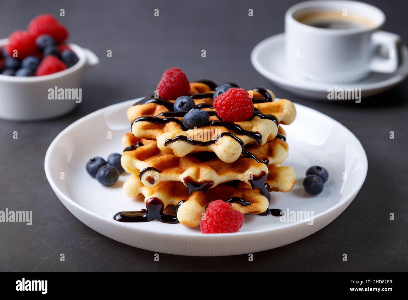 Waffle viennesi o belgi con bacche fresche (lamponi e mirtilli) su un piatto bianco e una tazza di caffè. Dessert tradizionale. Primo piano. Foto Stock