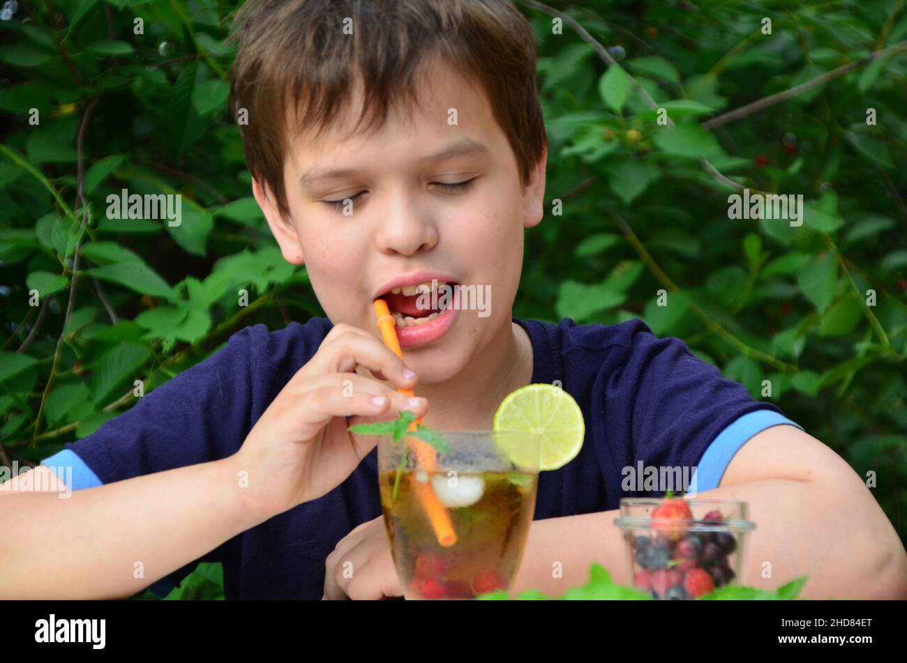 Bambino ragazzo drink naturale limonata bevanda estiva, tè con frutti di bosco, lime, lamponi e mirtilli, vacanza estiva nel parco. Rinfrescante naturale Foto Stock