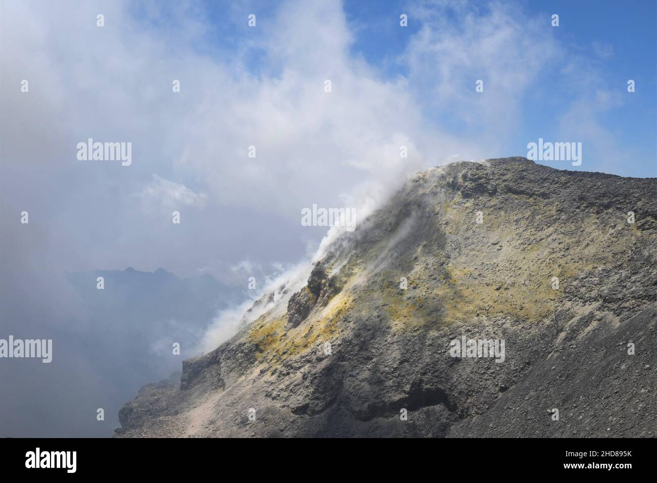 Cratere sommitale del vulcano Etna in Sicilia, Italia. Depositi di zolfo giallo (zolfo) sulle rocce grigie e marroni. Cielo blu con nuvole bianche. Foto Stock