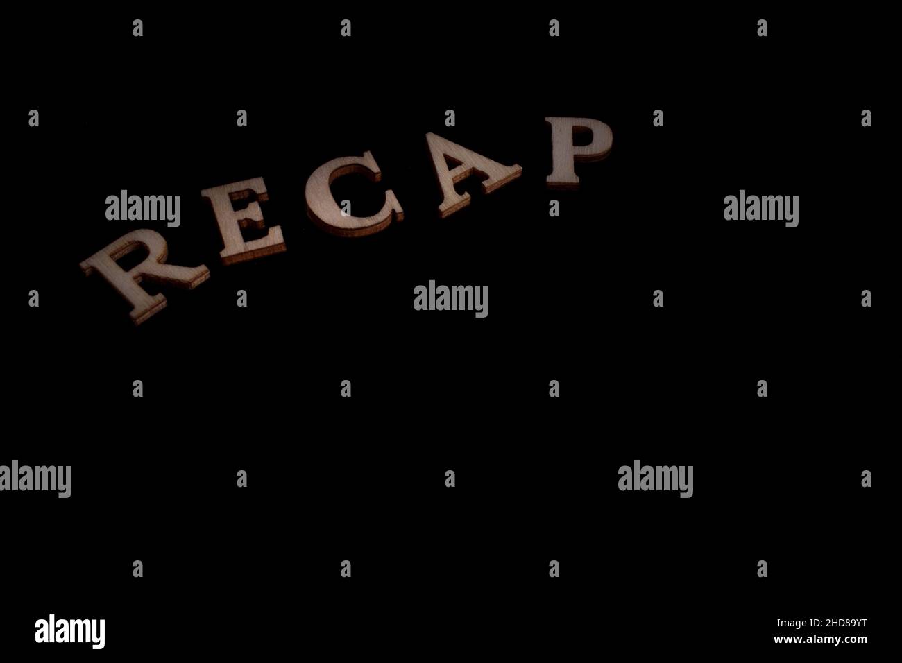 RICAPITOLARE parola fatta di lettere di legno isolato su sfondo nero - spazio di copia Foto Stock