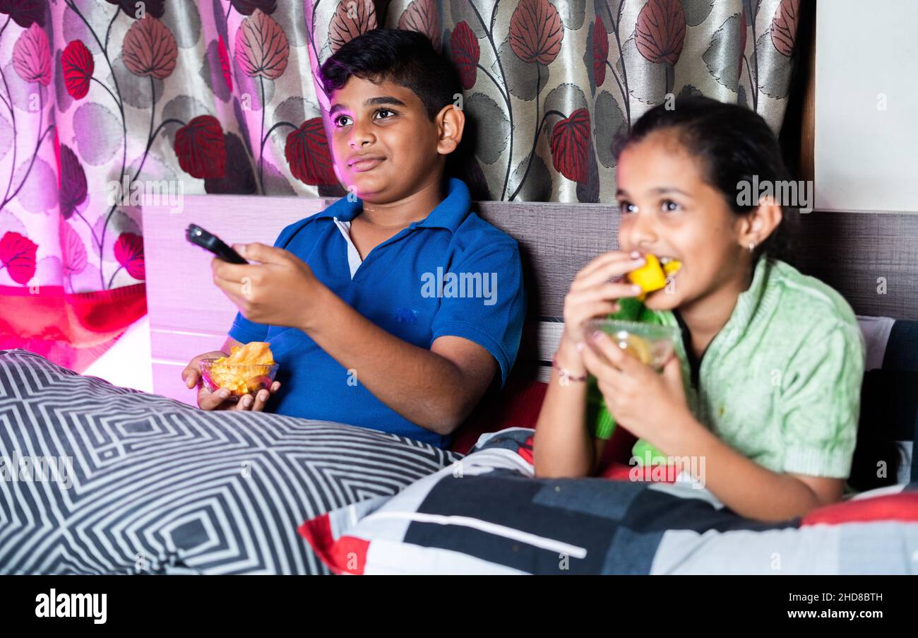 Focus su Boy, bambini in camera da letto occupato guardando online serie web in televisione o tv da avere snack durante la notte - concetto di cibo malsano Foto Stock