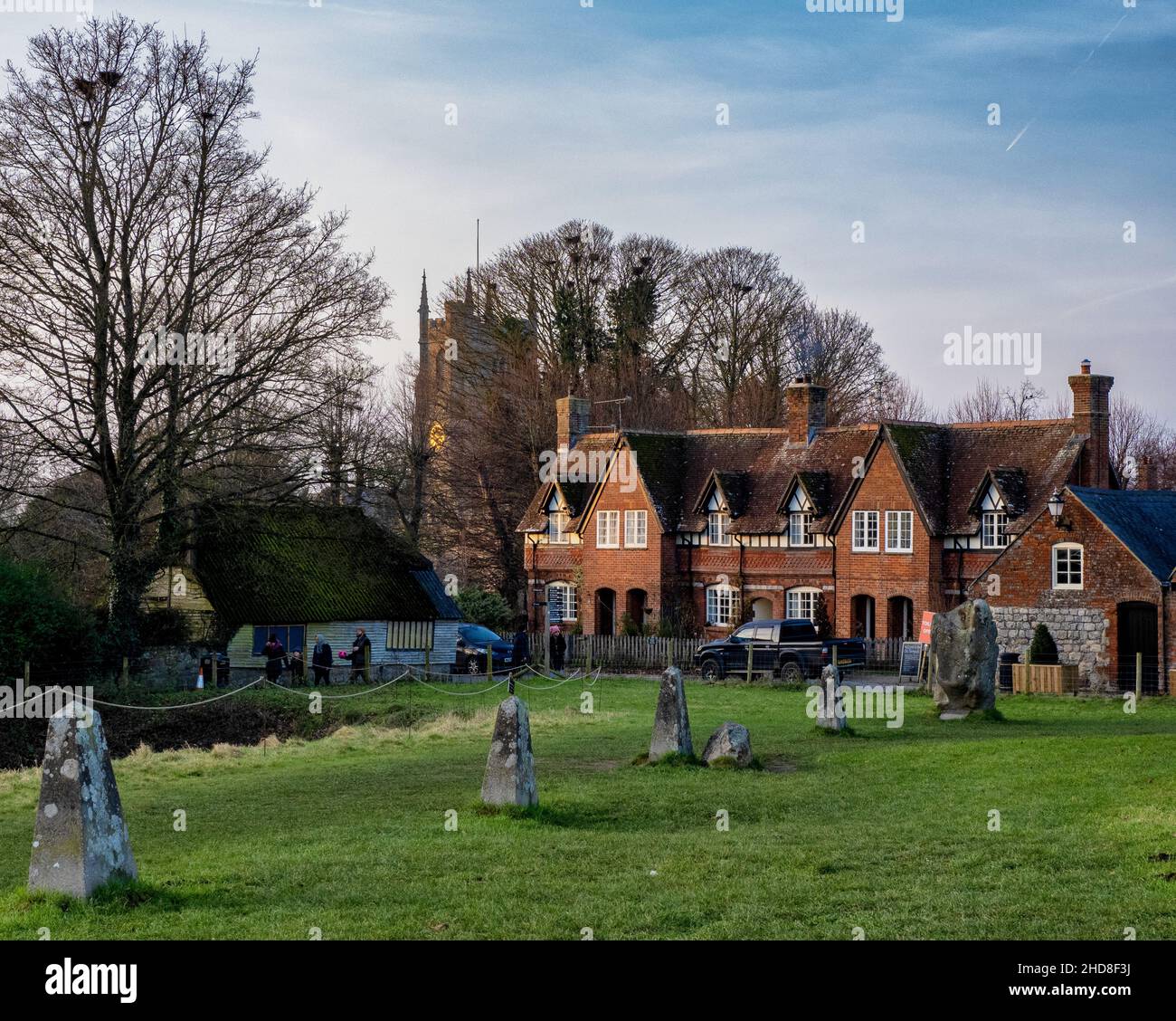 Vista invernale della chiesa di St James e cottage in mattoni in Avebury nel Wiltshire UK con pali di segnalazione di pietre mancanti in piedi del perimetro di henge Foto Stock