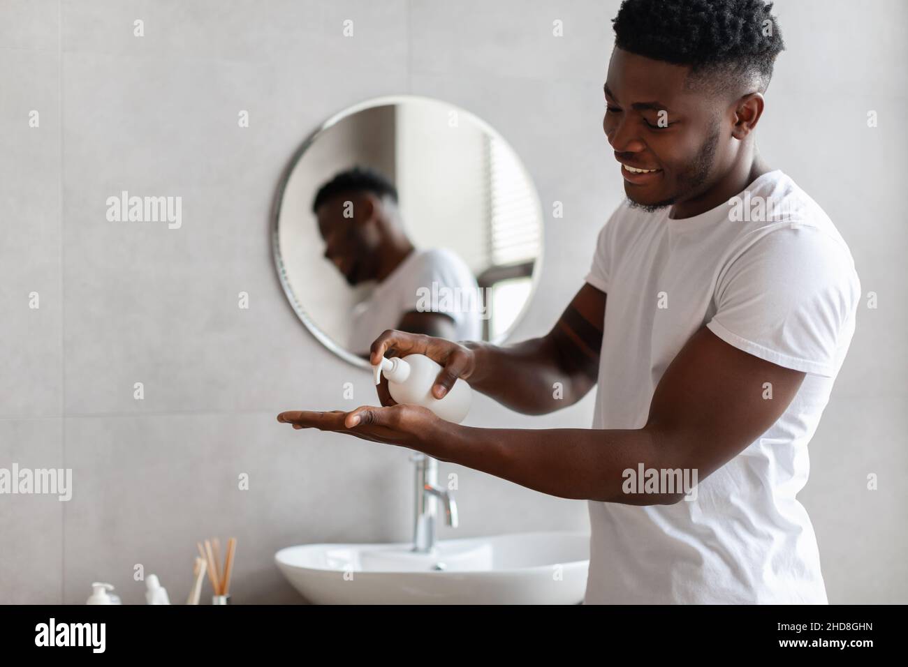African Man spremiando il sapone liquido dalla bottiglia in bagno Foto Stock