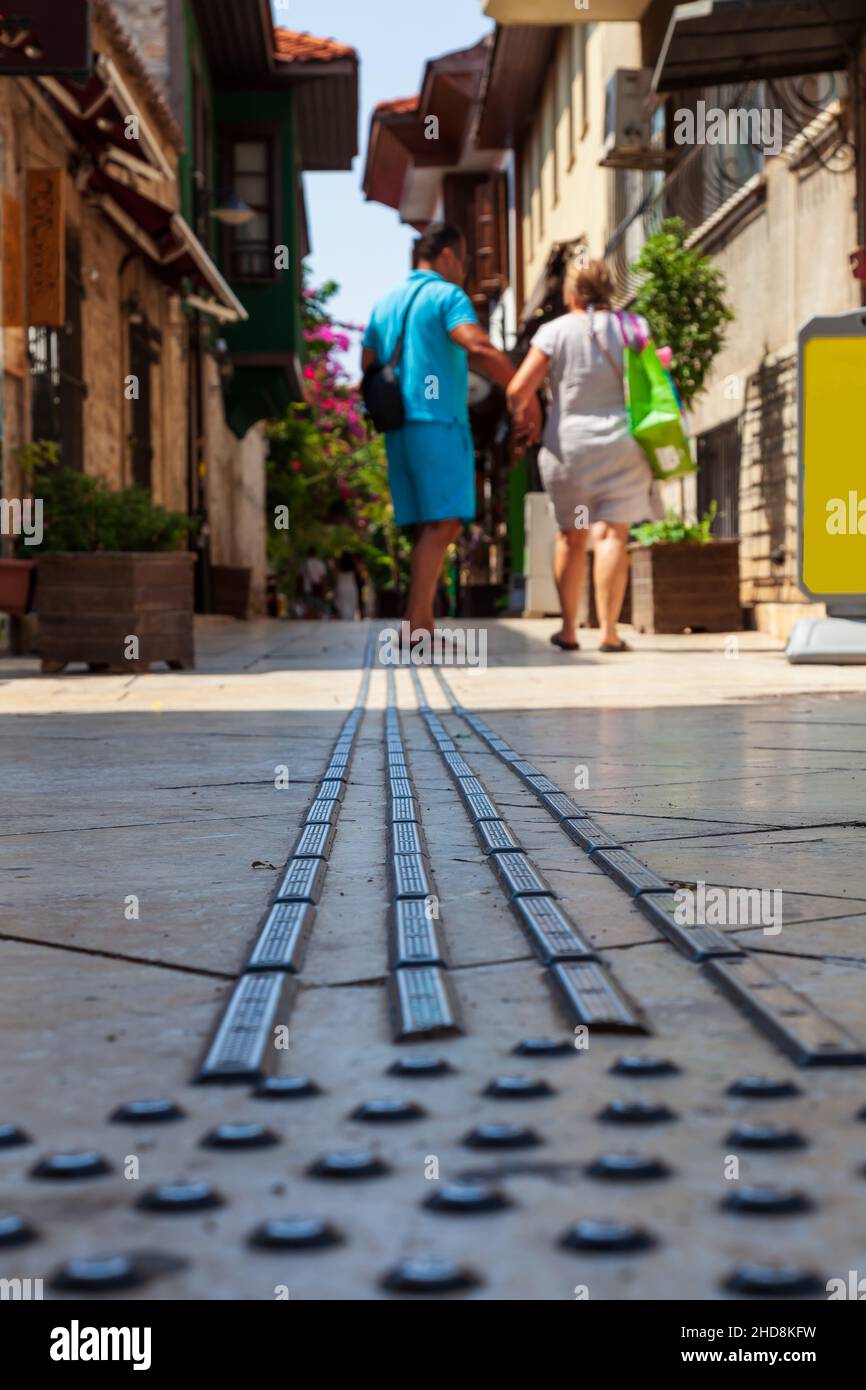 Una forma di struttura pubblica sul marciapiede è piastrelle disposte in una linea, per aiutare i non vedenti a camminare nella città vecchia di Alanya, Turchia. Fuoco di selecive. Foto Stock