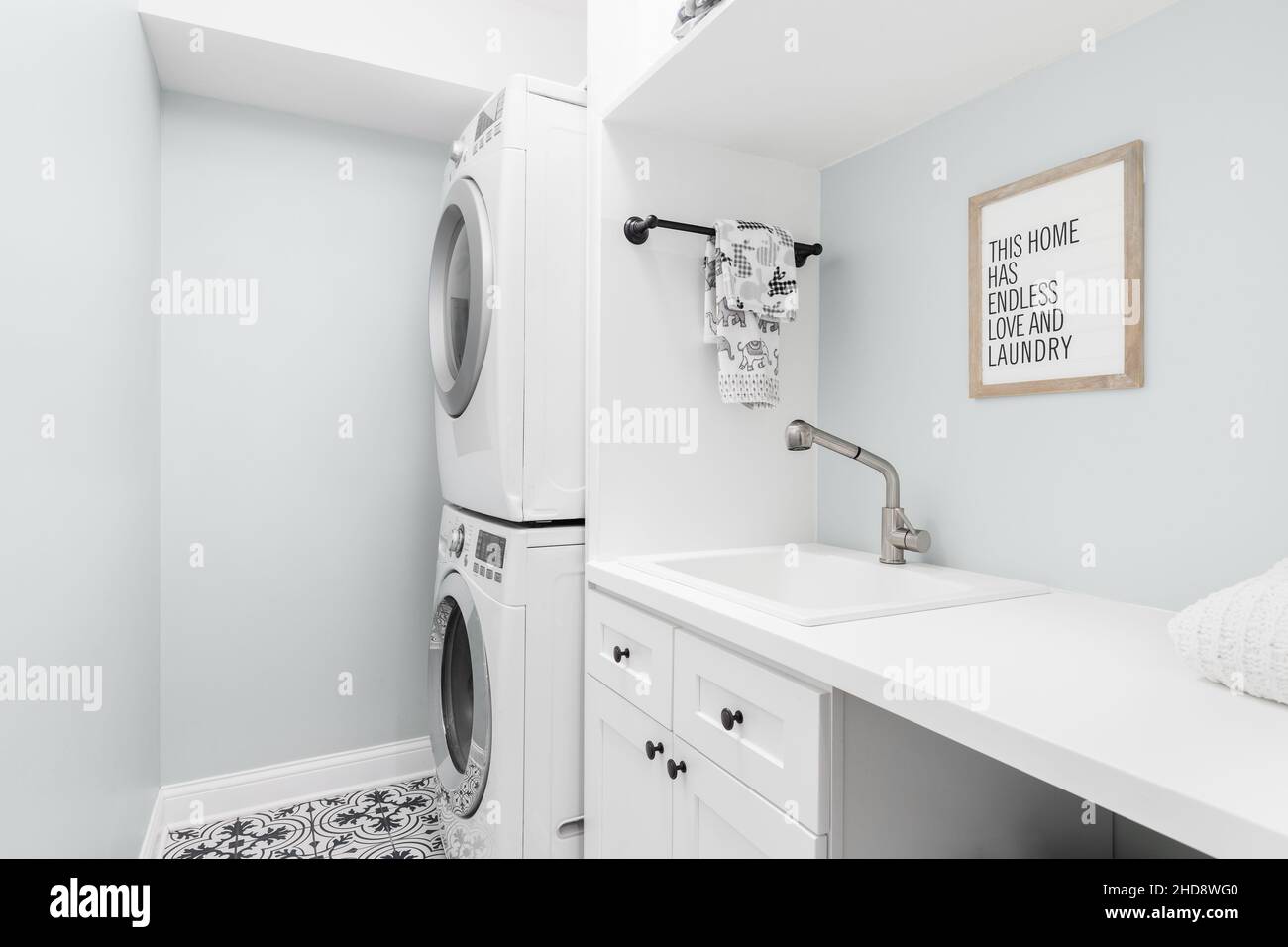 Una lavanderia rinnovata con pavimento piastrellato, armadietti bianchi, lavandino, lavatrice e asciugatrice bianca. Foto Stock