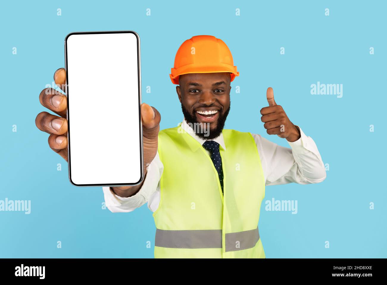Servizi di costruzione. Black Construction Worker che mostra uno smartphone vuoto e mostra il Thumb Up Foto Stock