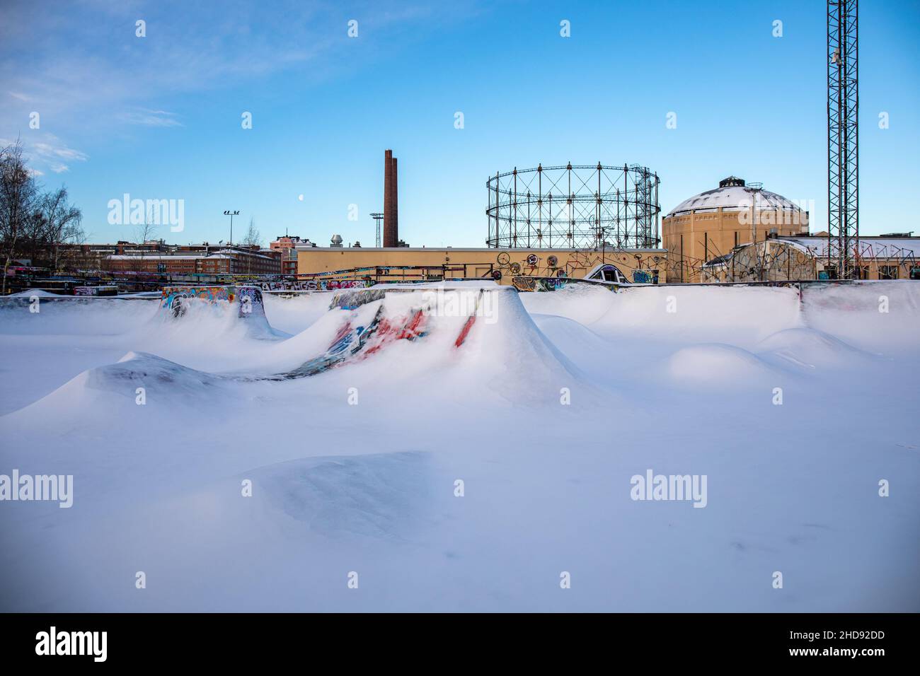 Suvilahti DIY Skate Park coperto di neve con i supporti di gas nel backroung a Helsinki, Finlandia Foto Stock