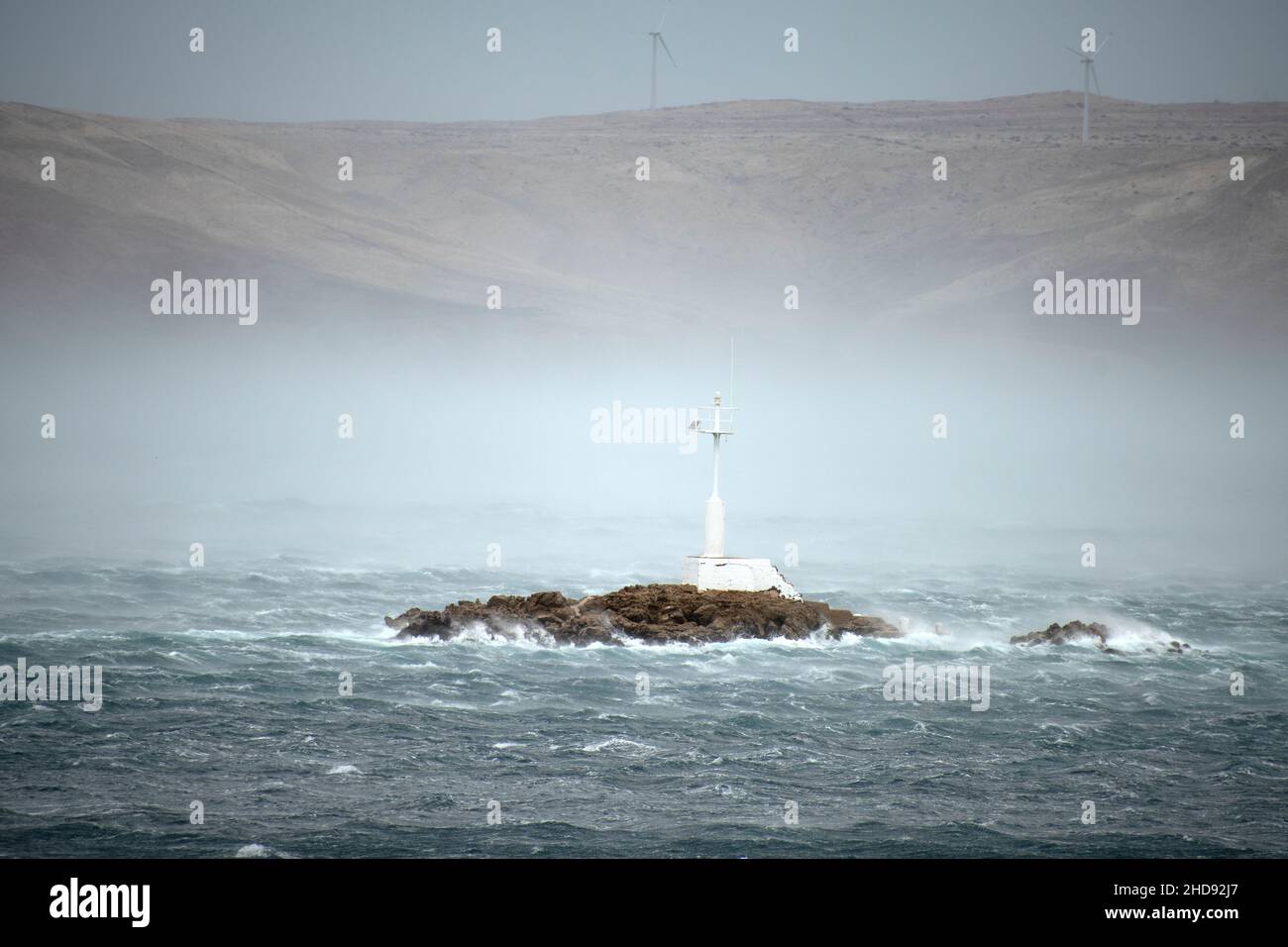 Faro bianco su un'isola rocciosa su un mare accidentato e suggestivo. Foto Stock