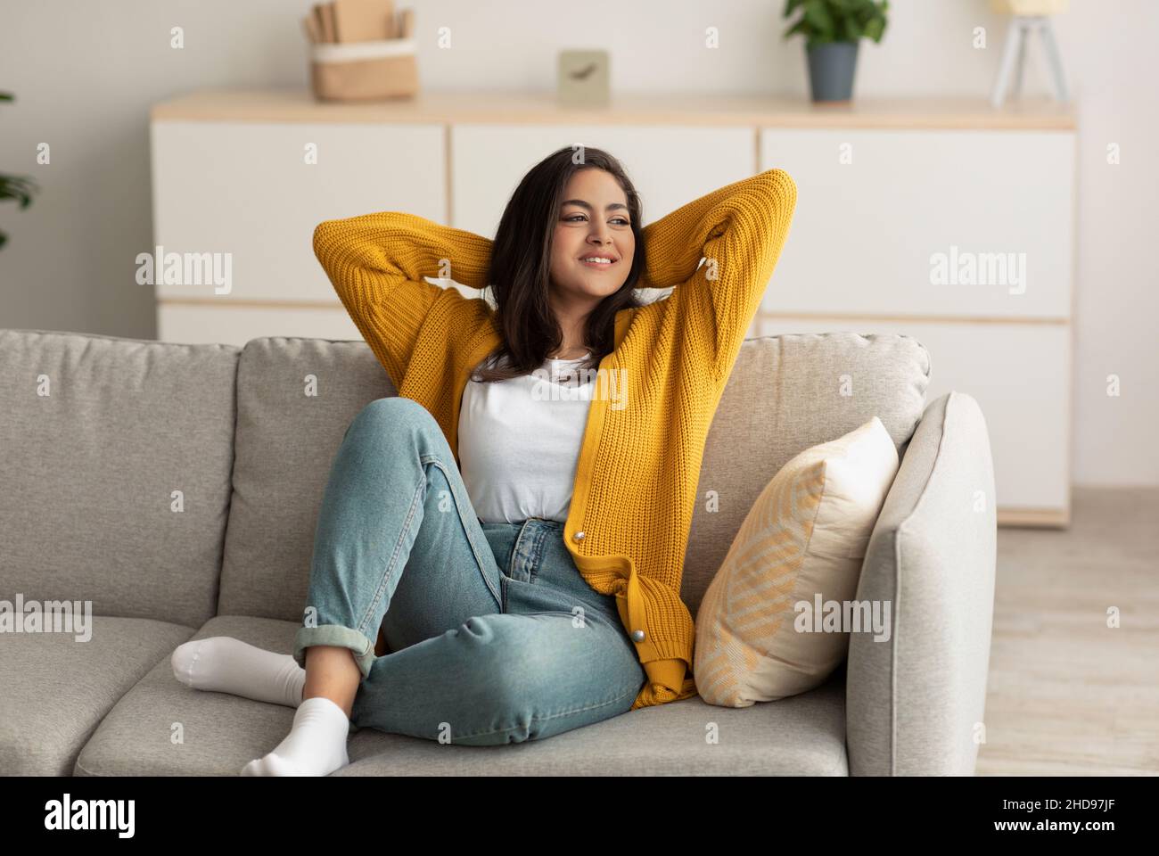Rimani a casa da solo e goditi il silenzio. Serena felice ragazza araba che riposa sul divano in un soggiorno minimalista Foto Stock
