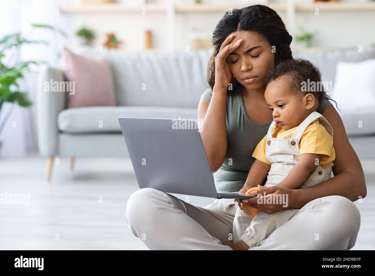 Madre nera stanca che ha problemi con il lavoro remoto mentre bambino del bambino del bambino del babysitter Foto Stock