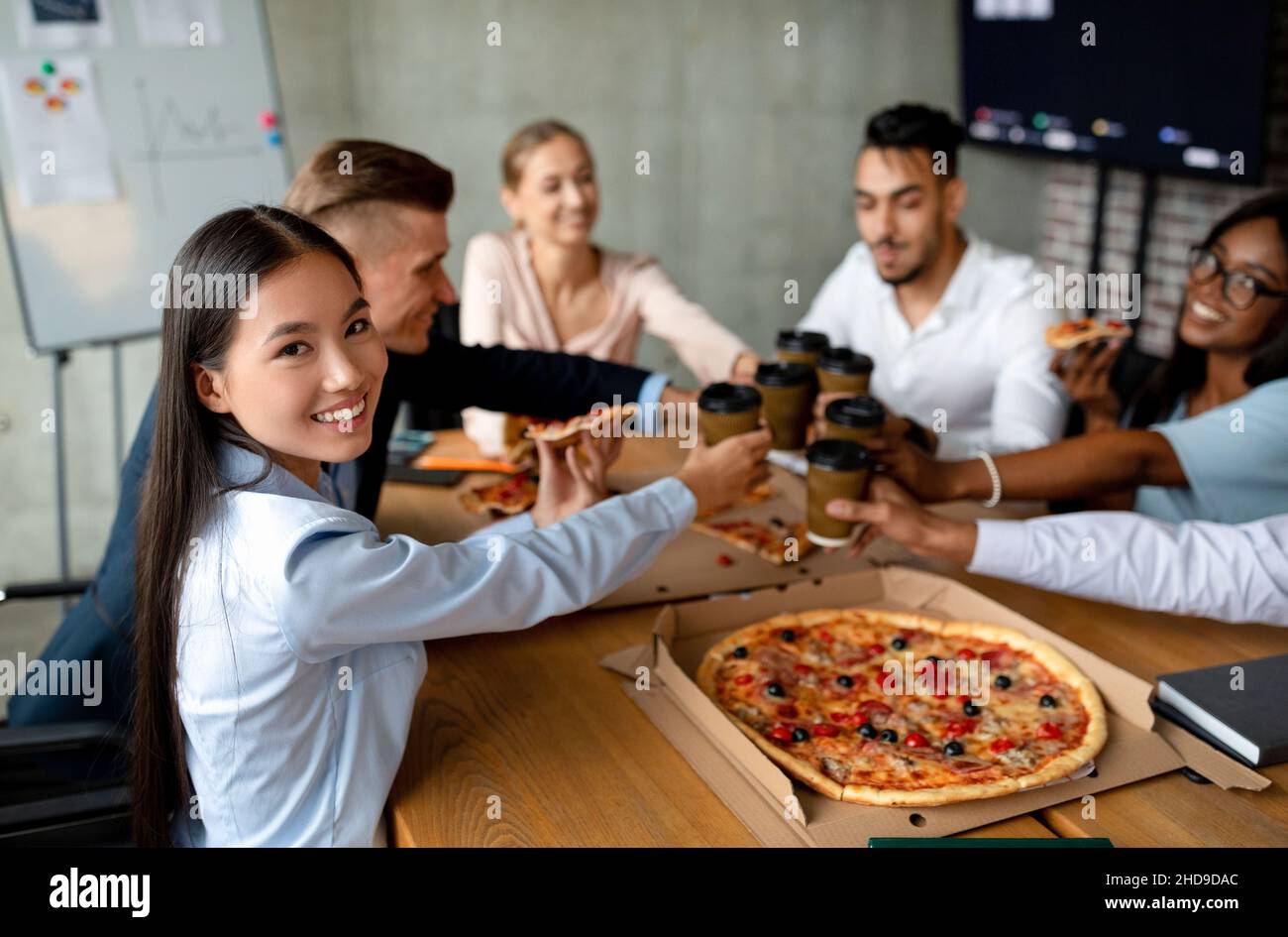 Festa in ufficio. Gruppo multietnico di colleghi bere caffè e mangiare pizza insieme Foto Stock