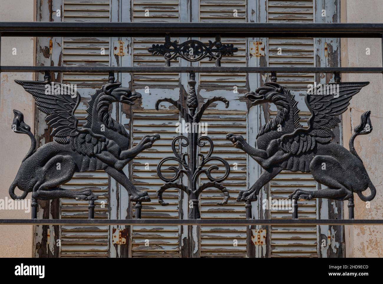 ghisa mitica creature griffins o draghi su ringhiere su un balcone architettonico su casa greca con shabby chic tempo persiane legno. Foto Stock