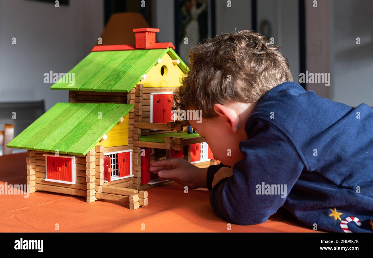 Bambino caucasico che gioca con una cabina vintage in legno di legno su un tavolo, un giocattolo creativo in legno da costruzione. Foto Stock