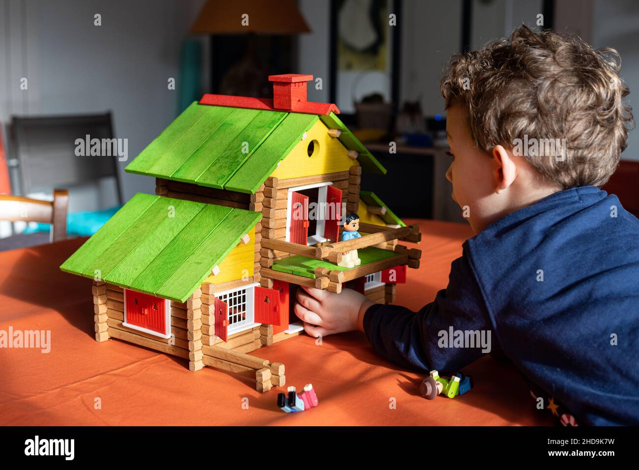 Bambino caucasico che gioca con una cabina vintage in legno di legno su un tavolo, un giocattolo creativo in legno da costruzione. Foto Stock