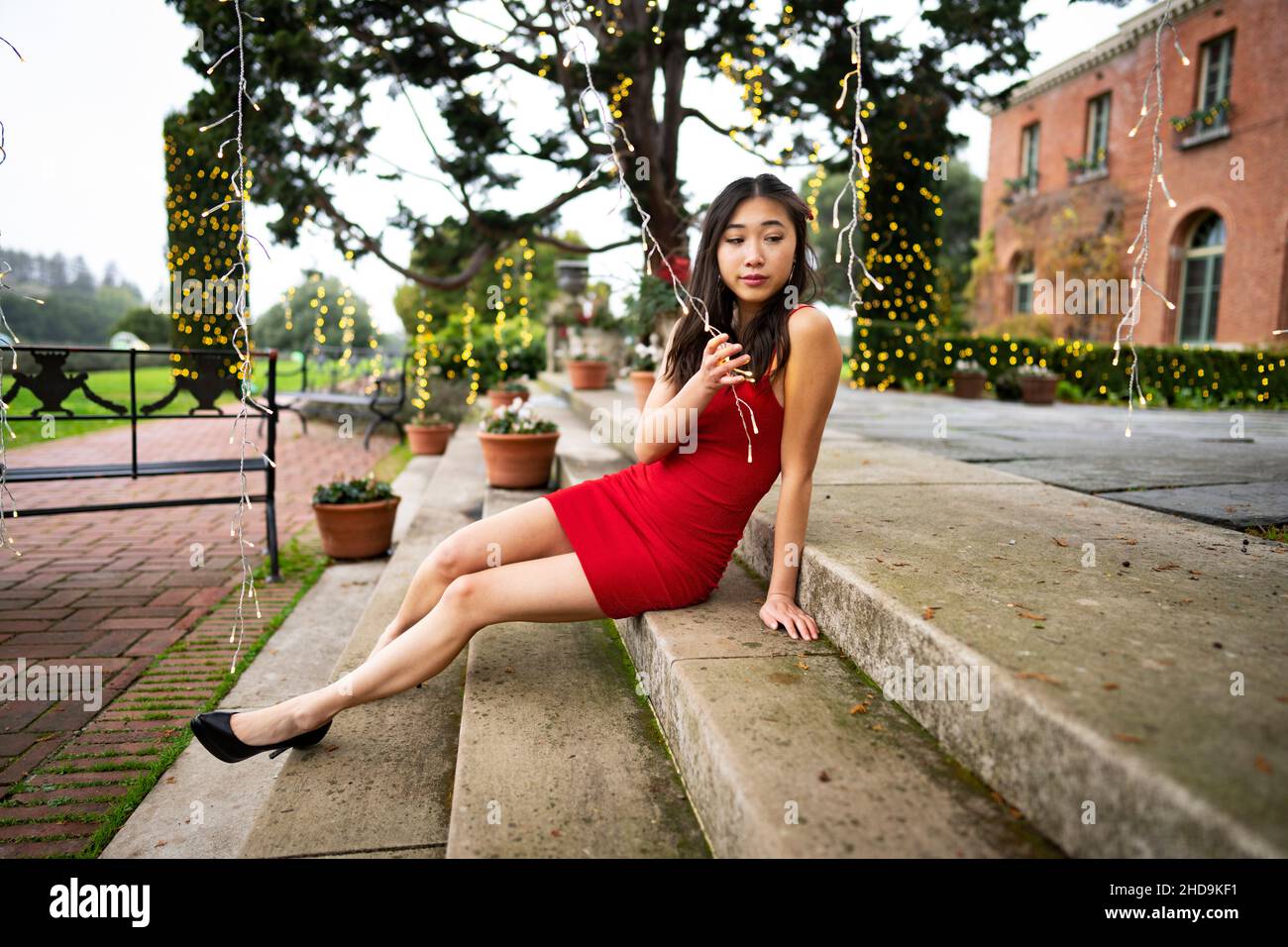 Giovane donna dell'Asia orientale in Red Party / vestito di festa che si rilassa su gradini giocando con le luci Foto Stock