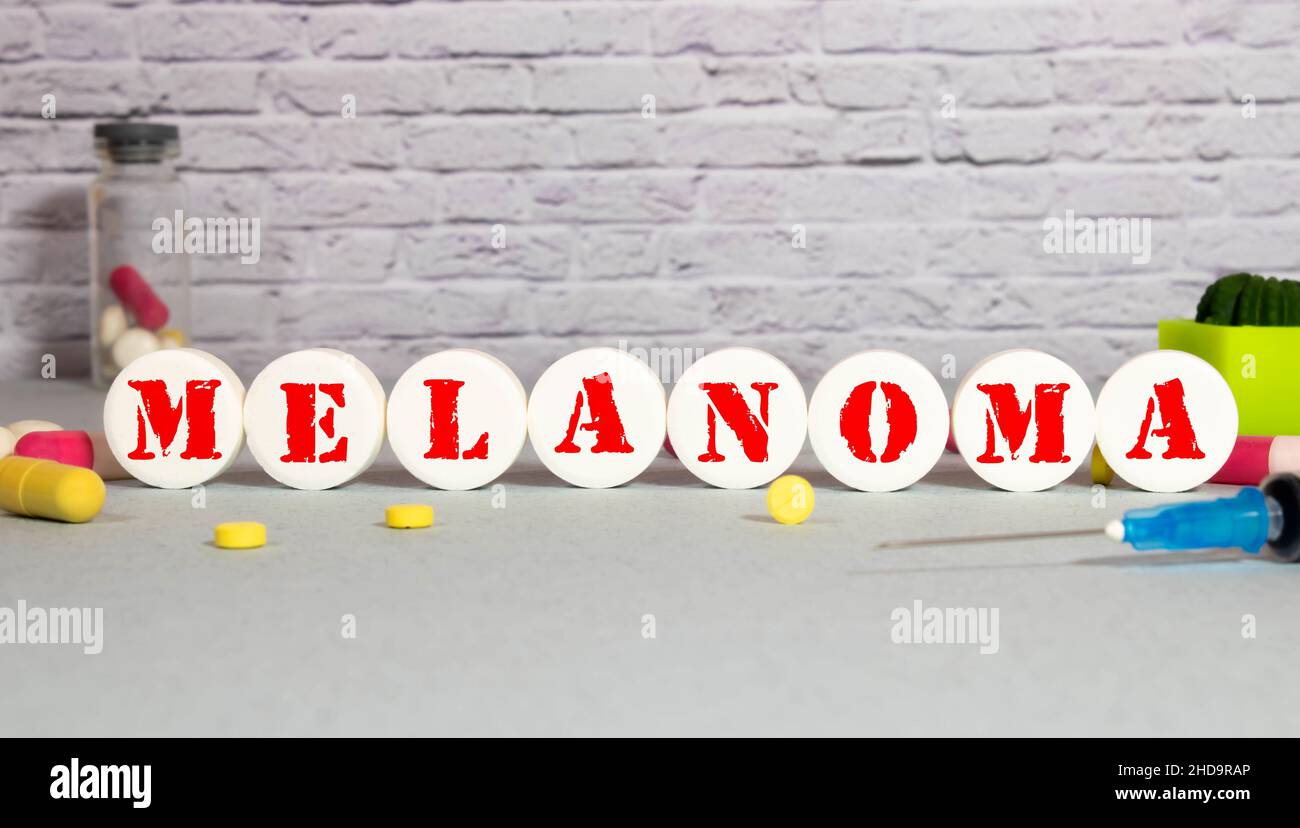 Su sfondo blu, uno stetoscopio, una siringa e pillole e un blocco di legno con la parola MELANOMA. Concetto medico Foto Stock