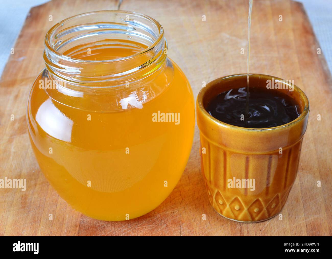 Miele biologico fresco naturale che viene versato in una piccola tazza rustica accanto ad un vaso pieno di miele. Foto Stock