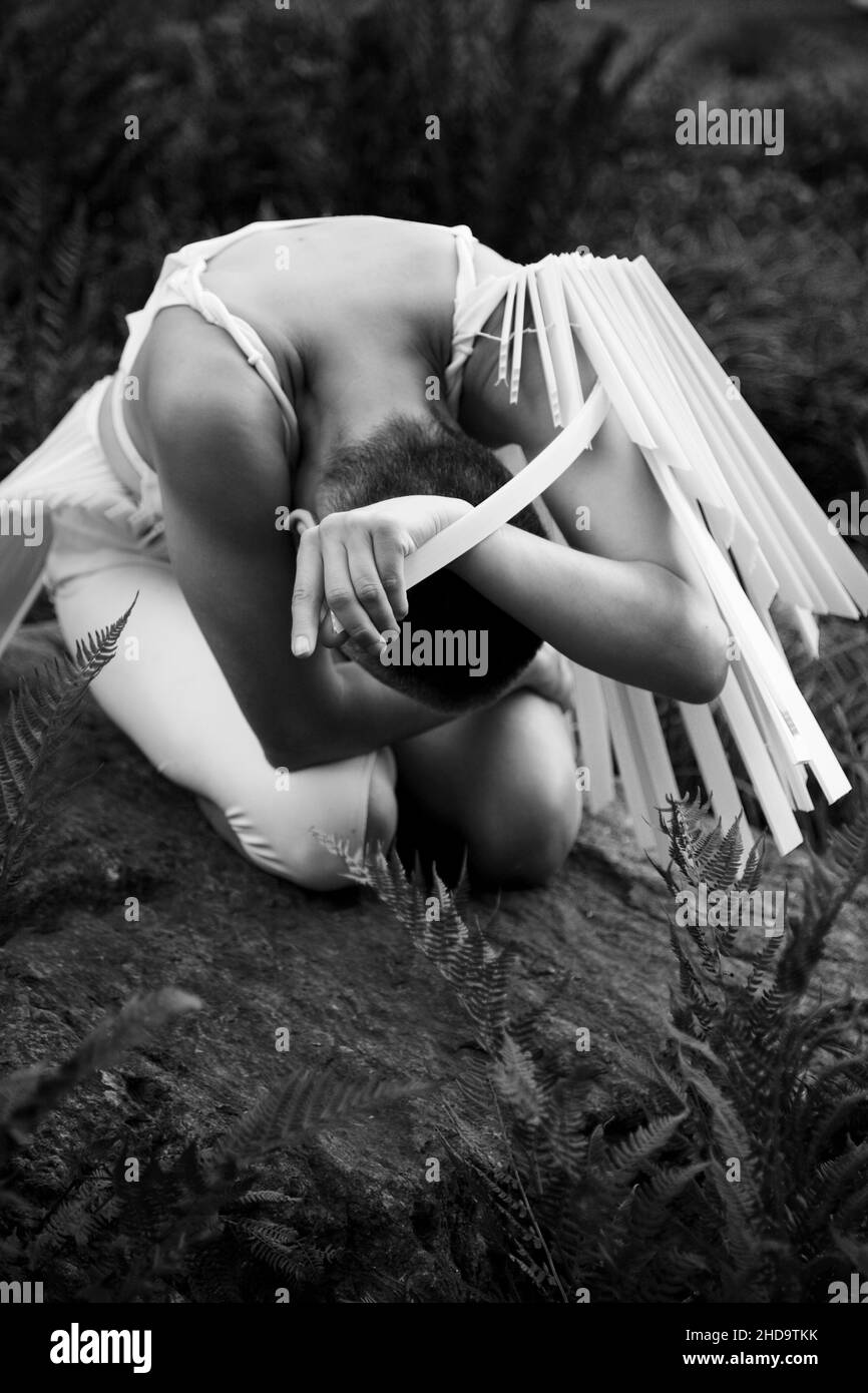 Ballerino femmina seduto in bianco piegandosi in avanti tra vegetazione Foto Stock