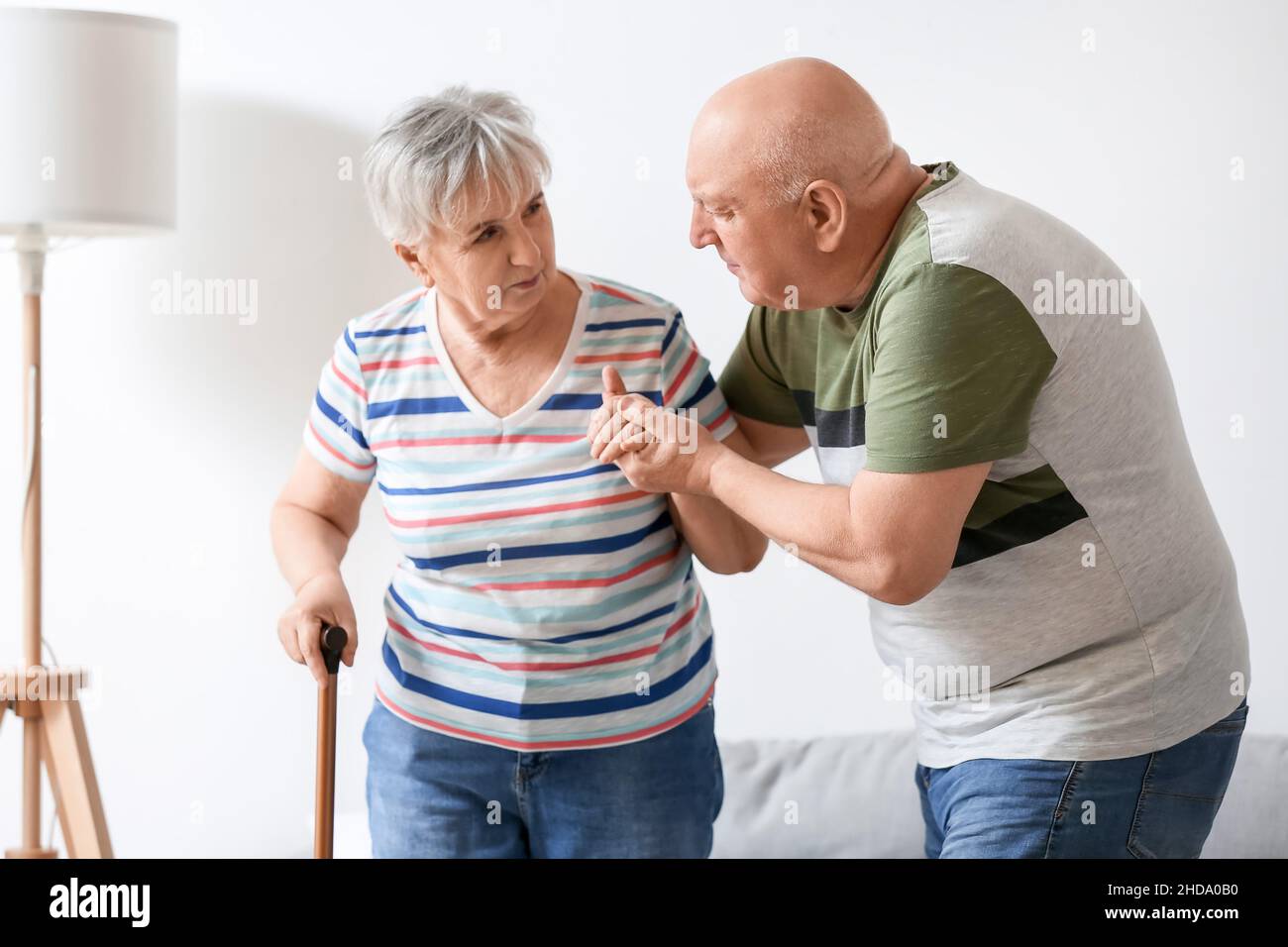 Uomo anziano che aiuta sua moglie con bastone a piedi a casa Foto Stock