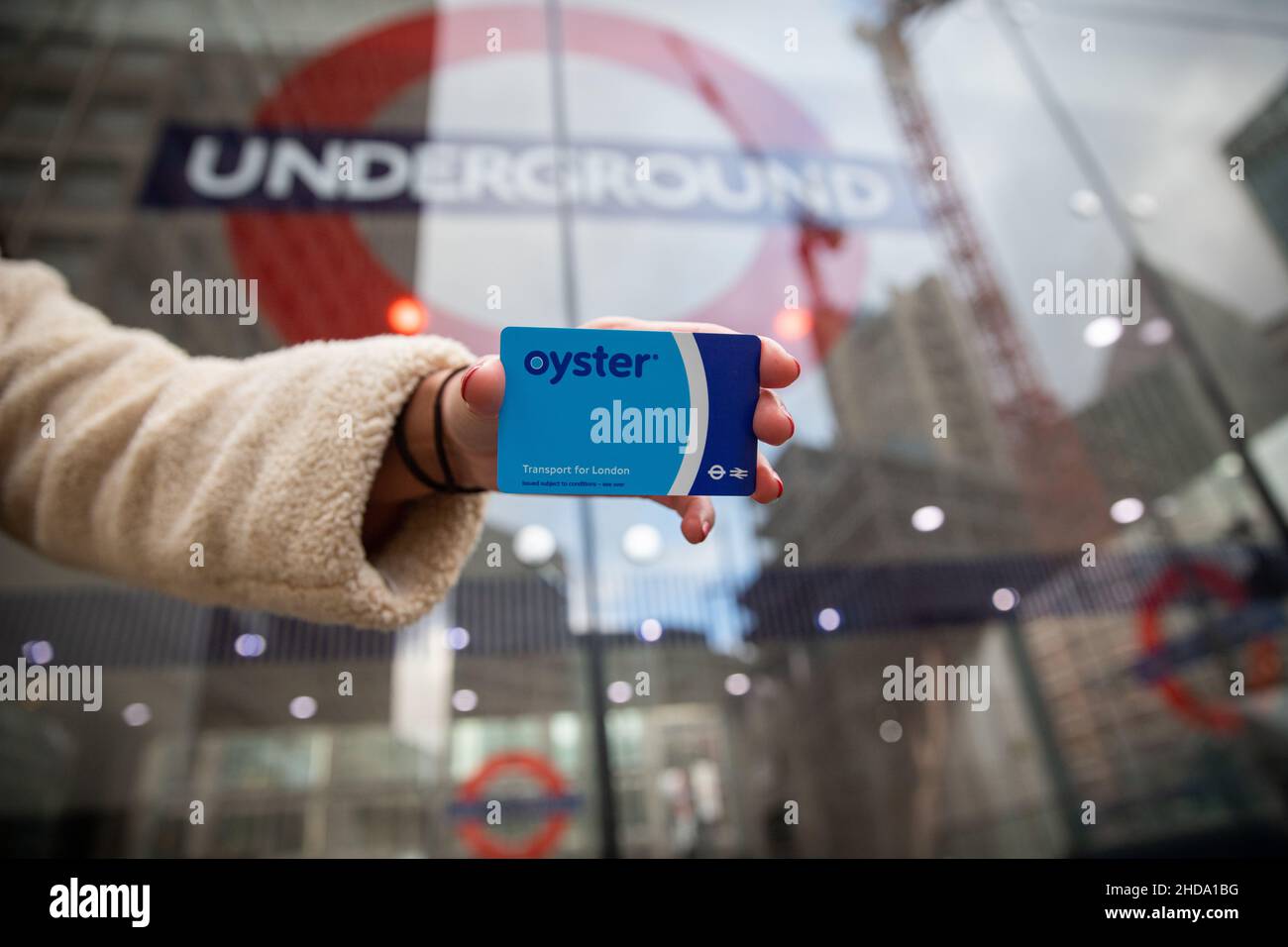 Mano di una ragazza che tiene una carta Oyster fuori dall'ingresso della metropolitana sullo sfondo. La carta consente l'accesso alla metropolitana di Londra, Foto Stock