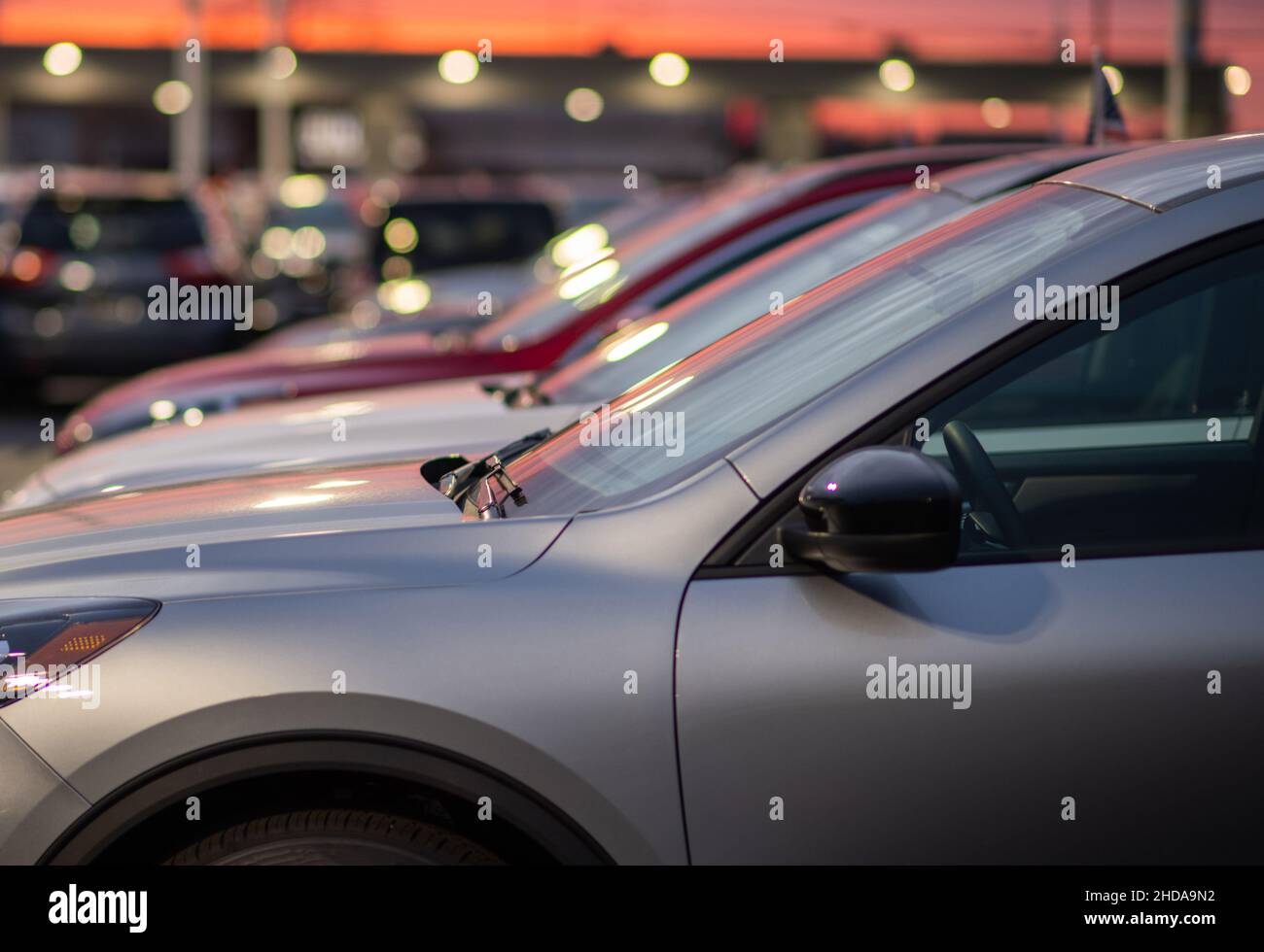 Nuovi veicoli compatti moderni disponibili a stock presso i concessionari. Tema commerciale vendite auto. Prima serata con luci di parcheggio artificiali. Concessionario del settore automobilistico. Foto Stock