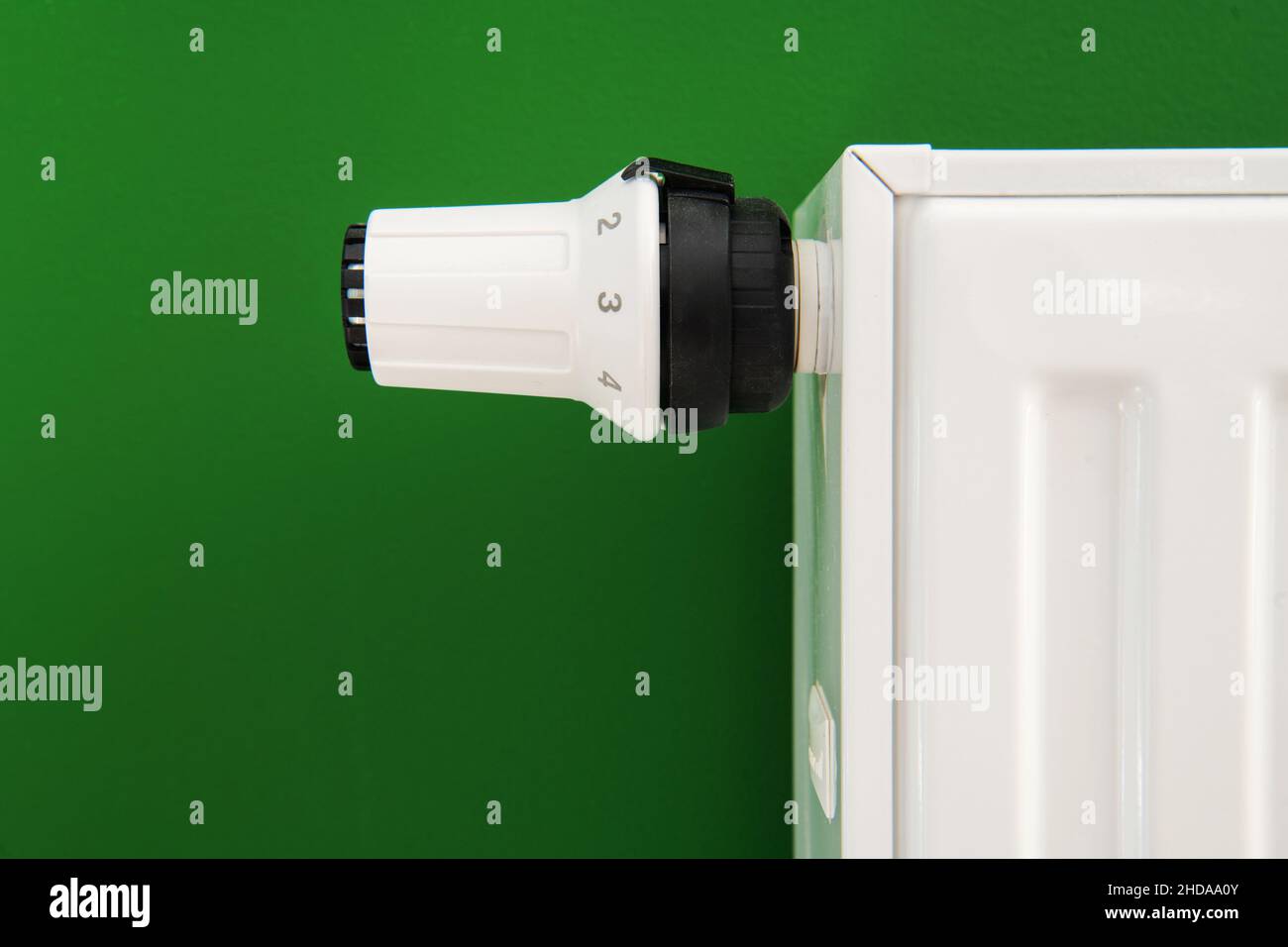 Chiusura della valvola del radiatore termostatico. Valvola di regolazione della temperatura del dispositivo di riscaldamento dell'impianto di riscaldamento ad acqua calda per uso residenziale. Muro verde scuro. Foto Stock