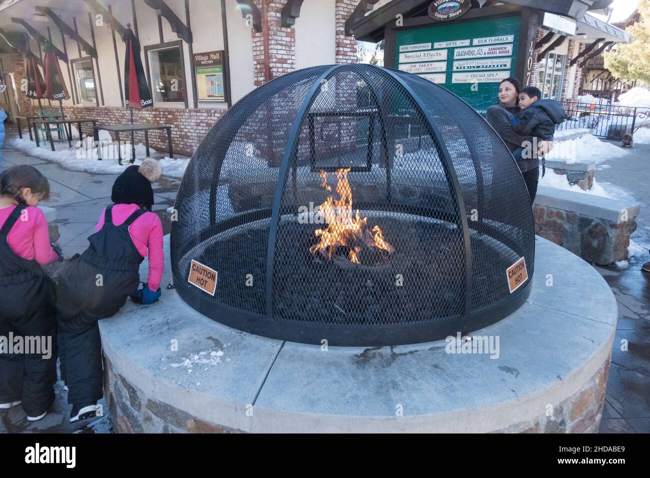 Persone che si riscaldano vicino alla fossa pubblica di fuoco sul marciapiede lungo il Village Dr a Big Bear Lake, California, USA Foto Stock