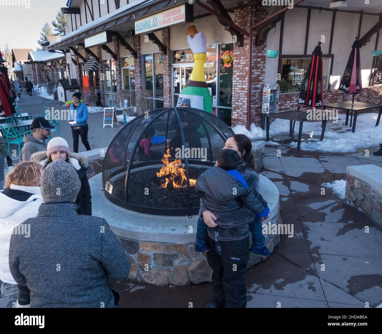 Persone che si riscaldano vicino alla fossa pubblica di fuoco sul marciapiede lungo il Village Dr a Big Bear Lake, California, USA Foto Stock