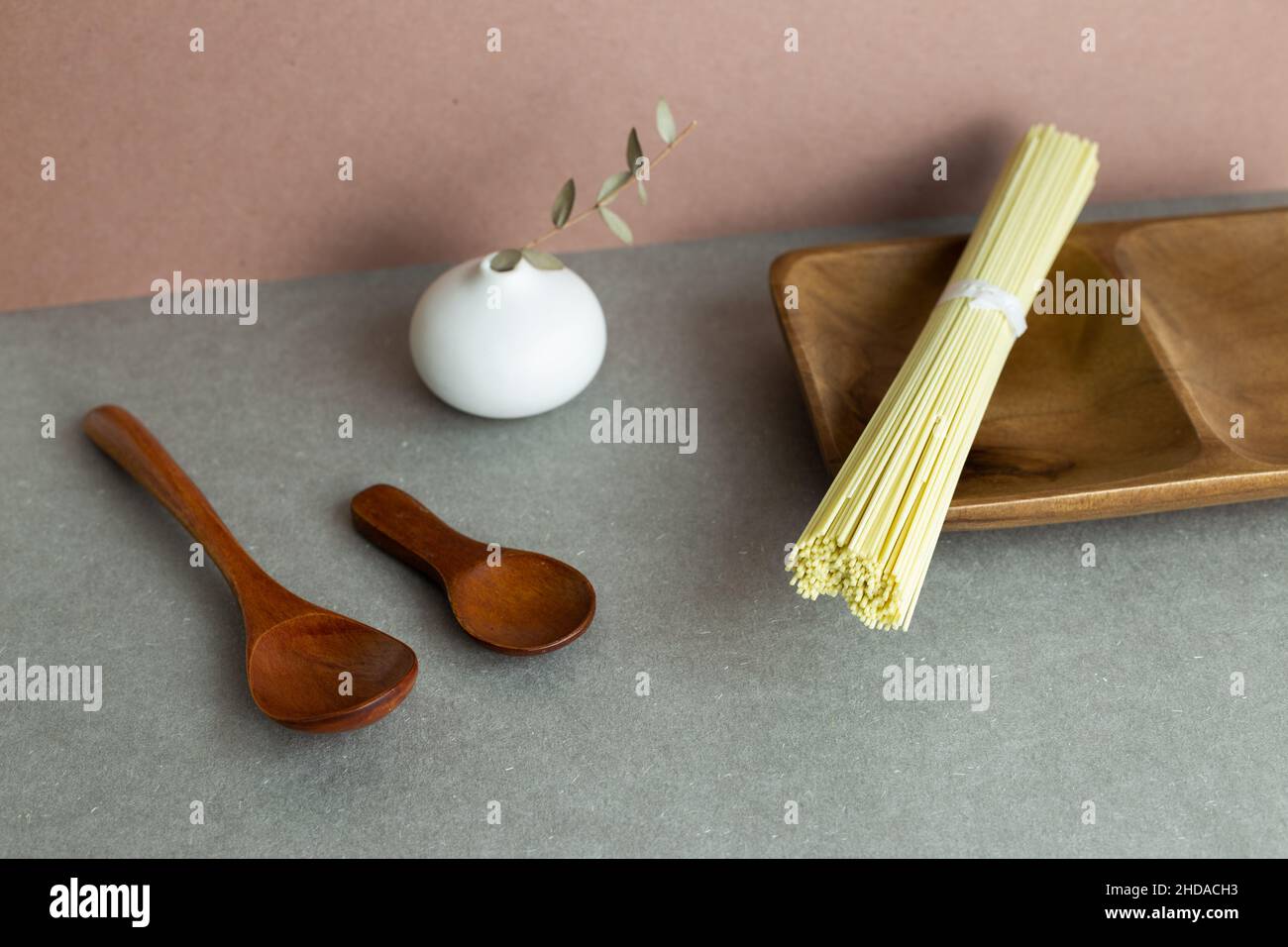 Still Life of Ramen noodles su vassoio di legno e vaso in ceramica e cucchiaio. Sfondo grigio Foto Stock