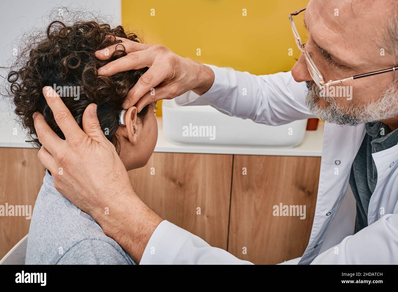 L'audiologo si adatta a un apparecchio acustico sull'orecchio maschile del bambino durante la visita a una clinica uditiva. Soluzioni per l'udito per bambini Foto Stock