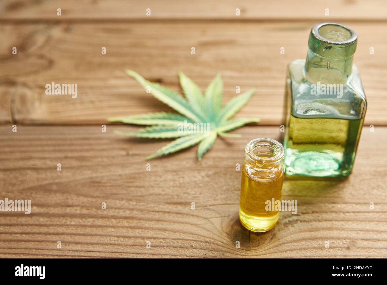 Olio di canapa in un vaso di vetro, foglie di canapa sullo sfondo di tavole di legno. Foto Stock