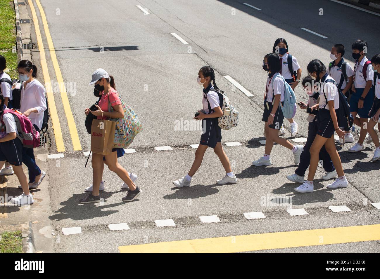 Vista aerea di un gruppo di bambini che attraversano la strada con maschere durante la pandemia. Singapore. Foto Stock