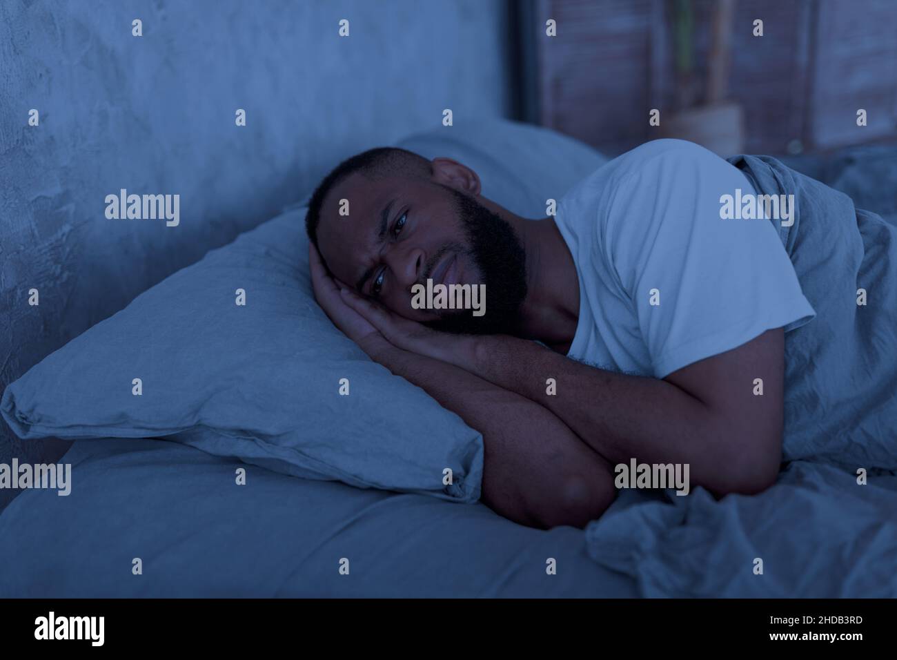 Uomo nero che si trova a letto e che pensa di notte Foto Stock