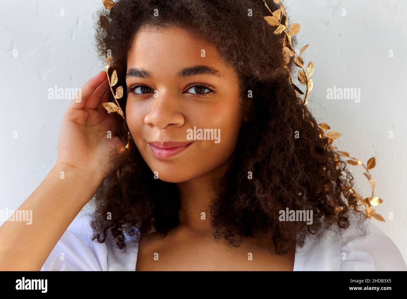 Primo piano ritratto di carina donna afroamericana con capelli ricci in oro foglia archetto guardando flirty fotocamera isolato su bianco, bella femmina con Foto Stock