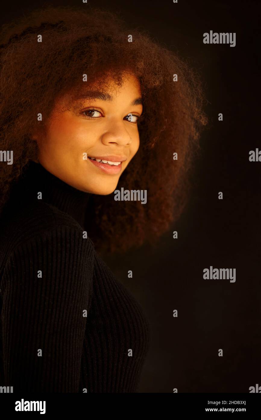 Ritratto di attraente sorridente donna afroamericana ricci in abiti neri guardando la macchina fotografica, posa isolata su sfondo scuro studio. Giovane Europa Foto Stock