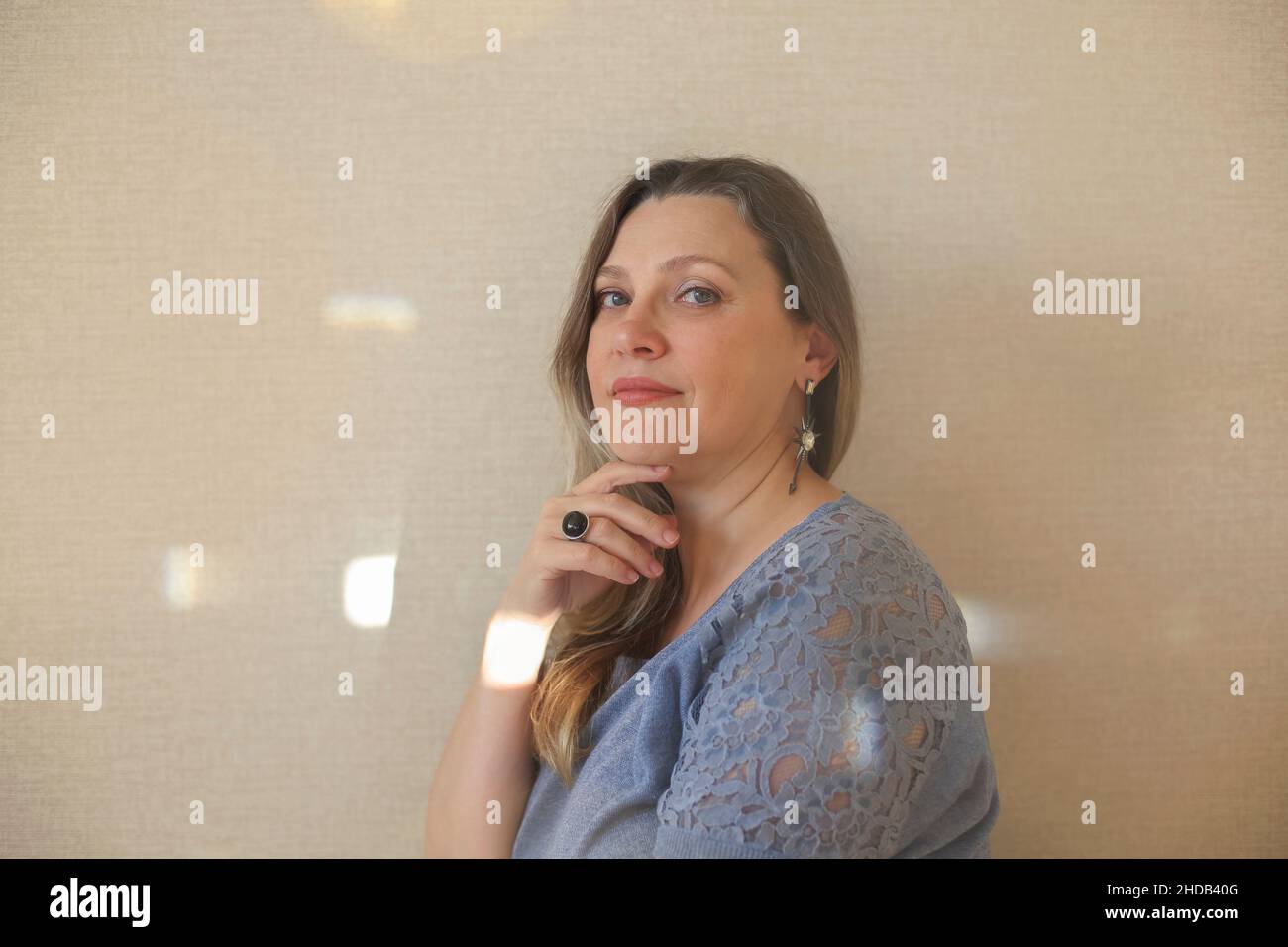 Amatevi ad ogni età. Donna di mezza età di 40s anni che tocca delicatamente il mento con la mano e guarda la macchina fotografica mentre si posa isolato su sfondo beige chiaro Foto Stock