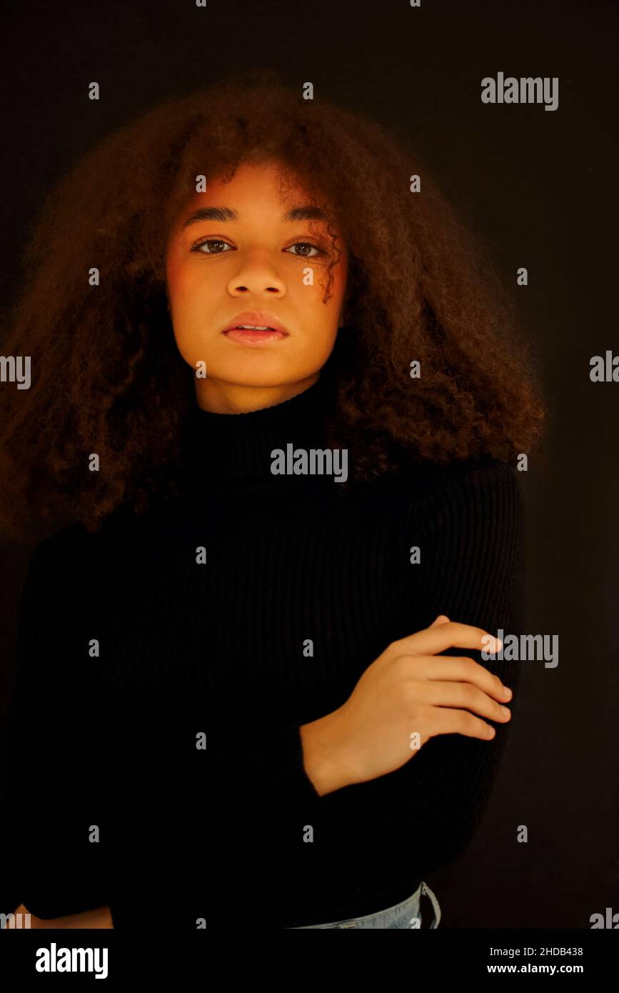 Ritratto di attraente sorridente donna afroamericana ricci in abiti neri guardando la macchina fotografica, posa isolata su sfondo scuro studio. Giovane Europa Foto Stock