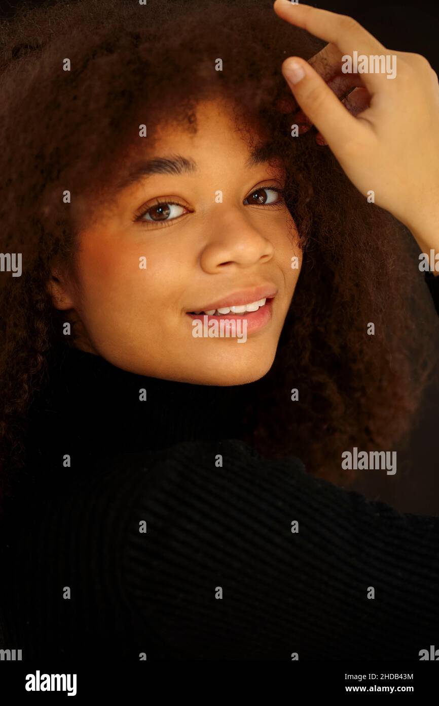 Ritratto di attraente sorridente donna afroamericana ricci in abiti neri guardando la macchina fotografica, posa isolata su sfondo scuro studio. Giovane Europa Foto Stock